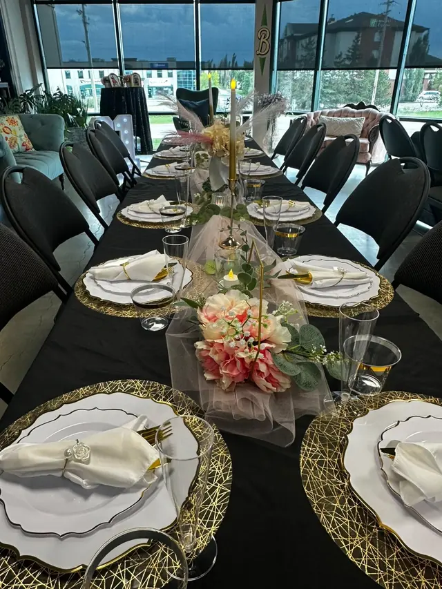 A birthday table with black linen, gold chargers and a pink floral centrepiece