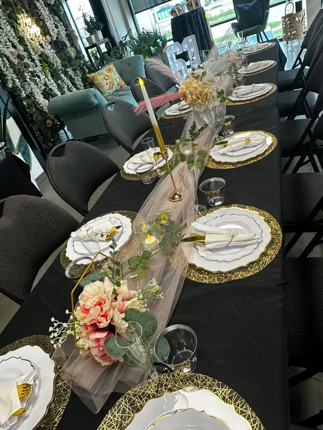 A long black-linen birthday table with gold chargers, a pink floral centrepiece and a tall gold candle
