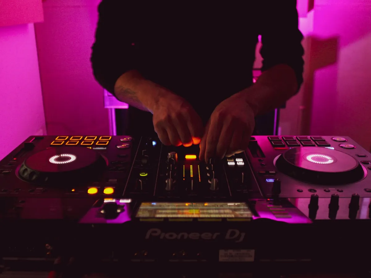 A DJ's hands on a Pioneer controller under magenta light